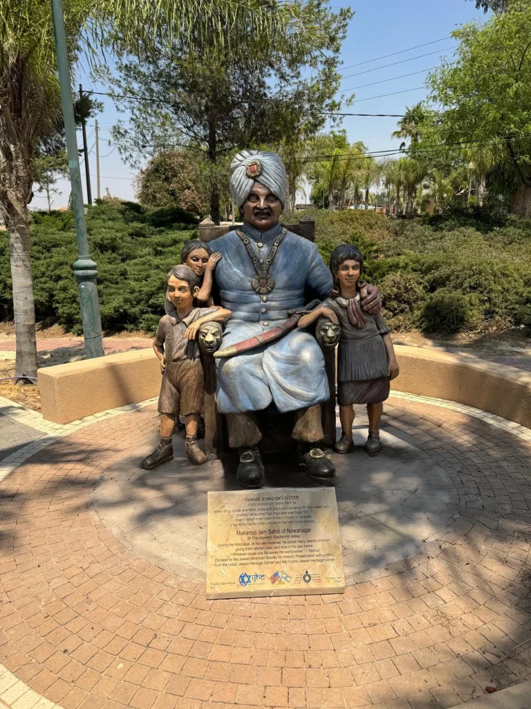 המהרג׳ה ג׳אם סאהיב יושב בכיסא בלבוש מסורתי ובטורבן, מוקף בשלוש דמויות ילדים; הפסל בנבטים