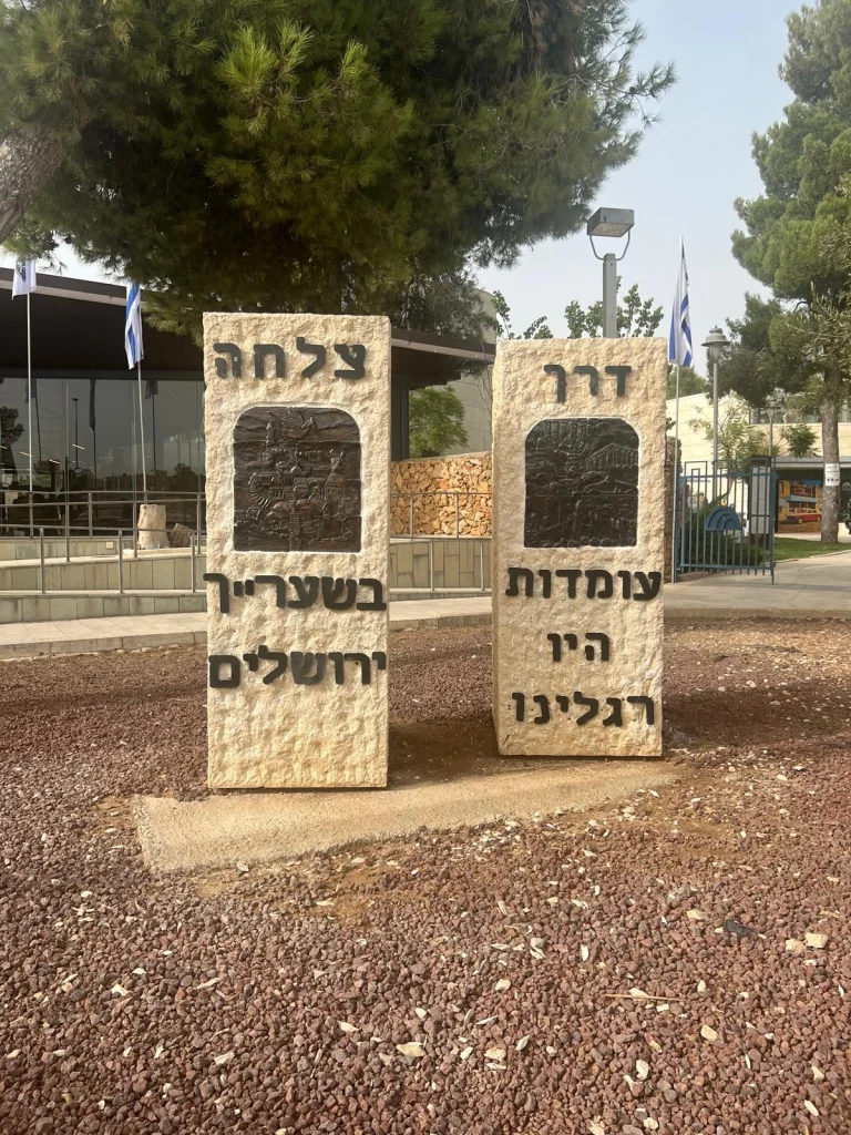 שתי אבנים ירושלמיות זו לצד זו עם המילים ״דרך צלחה״, תבליטי ברונזה ושורות מהפסוק ״עומדות היו רגלינו בשעריך ירושלים״