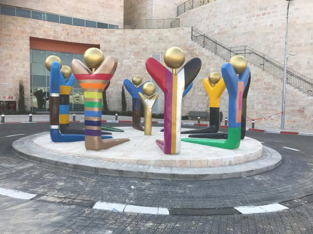 עשר דמויות מופשטות וצבעוניות במעגל סביב דמות ילד, בכניסה למרכז שלוה בירושלים